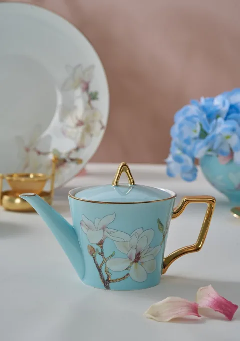 A blue floral ceramic teapot styled beside blue hydrangeas and coordinated tableware.