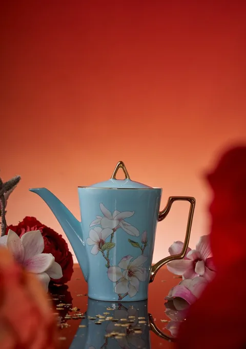 A tall blue floral ceramic cup styled against an orange-red background.