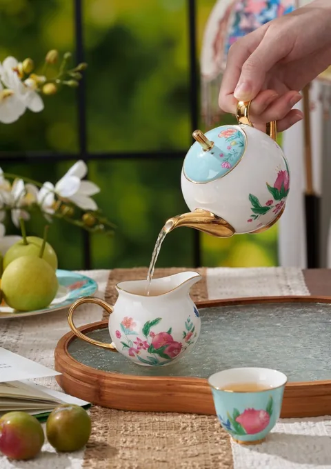 Tea poured from a decorated ceramic teapot into a matching cup in a garden-inspired setting.