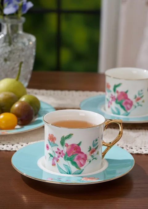 A floral ceramic cup and matching saucer with tea, fruit and soft window light.
