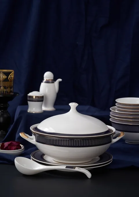 A covered white ceramic serving dish with a dark patterned rim against a deep blue backdrop.