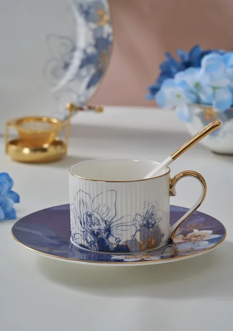 A white and blue illustrated ceramic teacup with a matching saucer and spoon.