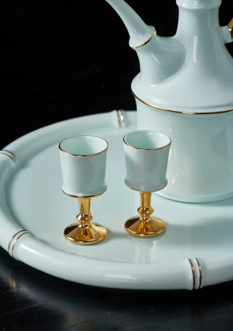 Small pale blue ceramic cups with gold-coloured bases arranged on a coordinated serving tray.