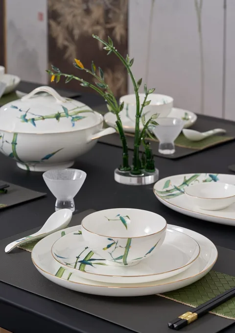 A white ceramic dinner setting with green bamboo motifs, including plates and a covered serving dish.