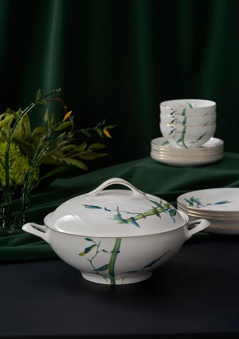 A bamboo-pattern covered ceramic dish with matching cups and foliage on a green table setting.