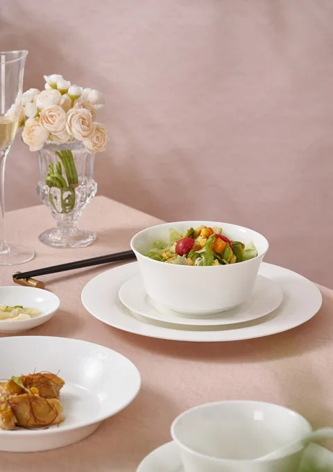 White ceramic bowls and plates arranged with food in a warm neutral dining scene.