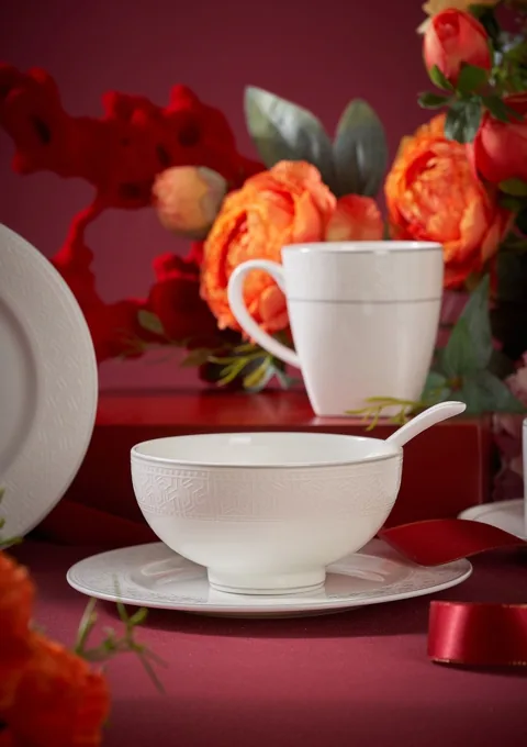 White ceramic cups and a covered vessel styled with vivid red flowers.