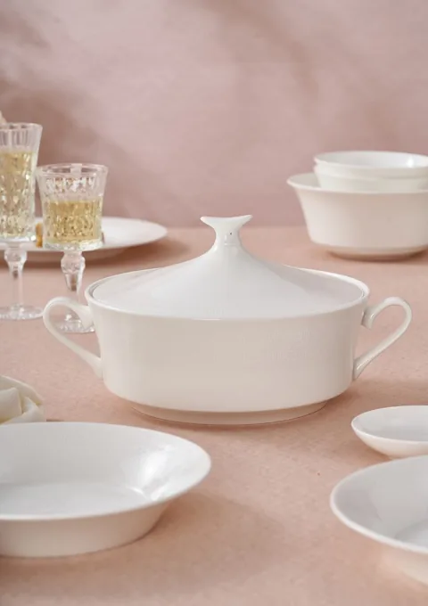 A white ceramic covered serving dish and coordinated tableware on a neutral table.