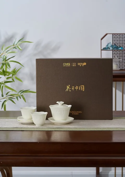 A white ceramic tea service displayed beside its dark presentation box and decorative bamboo.