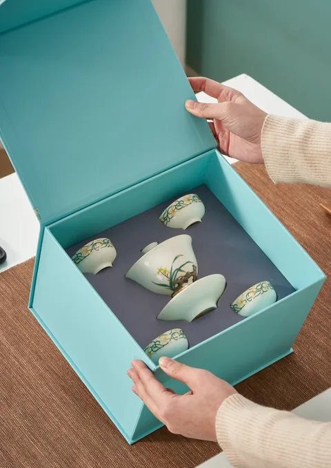 An open turquoise gift box presenting a coordinated ceramic tea set.