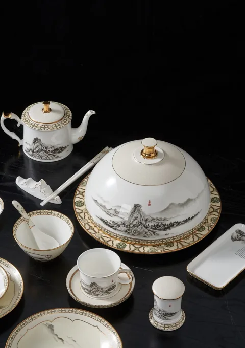 A white ceramic dinner service with ornate dark and gold-coloured details against a black backdrop.