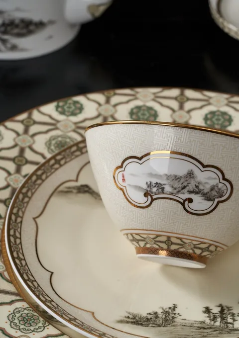 A close-up of a ceramic cup and plate with coordinated ornamental borders.
