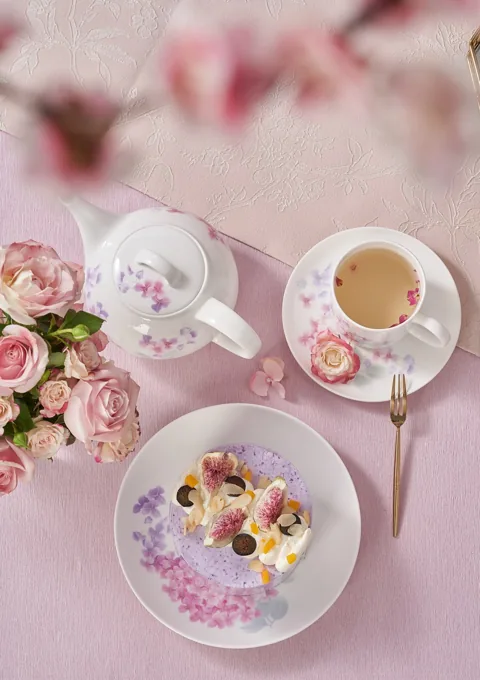 An overhead arrangement of pink floral ceramic tea pieces, flowers and a small dish.