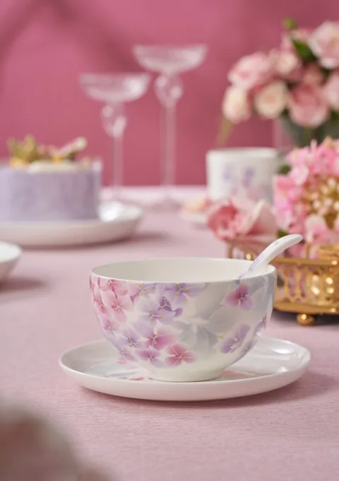 A pink floral ceramic cup and saucer in a softly styled tea-table scene.