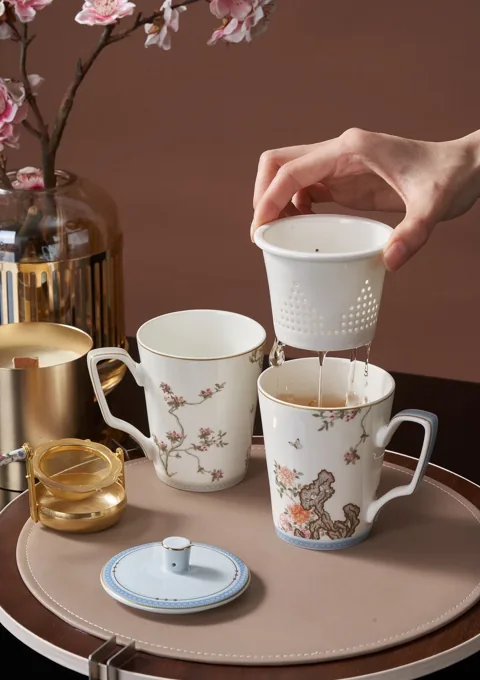 Decorated ceramic mugs with lids shown in a styled tabletop scene.