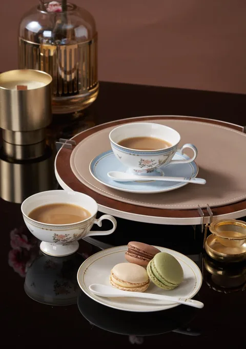 A coffee-table arrangement with ceramic cups, saucers and pastries in warm light.