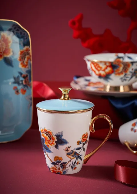 A colourful floral ceramic mug with a gold-coloured rim in a rich red composition.