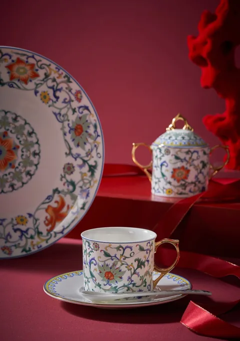 A floral ceramic cup, saucer and decorative plate styled against a red background.