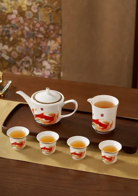 A ceramic teapot and matching cups with warm red decorative motifs in a traditional-inspired setting.