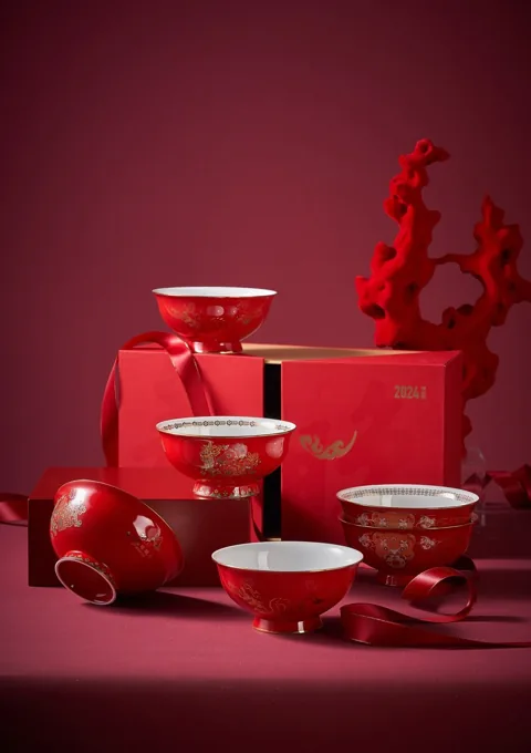 A red and white ceramic dinnerware collection with gift packaging and a festive backdrop.