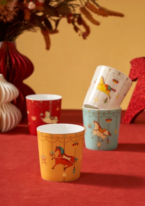 Colourful illustrated ceramic mugs arranged in a red and orange festive setting.