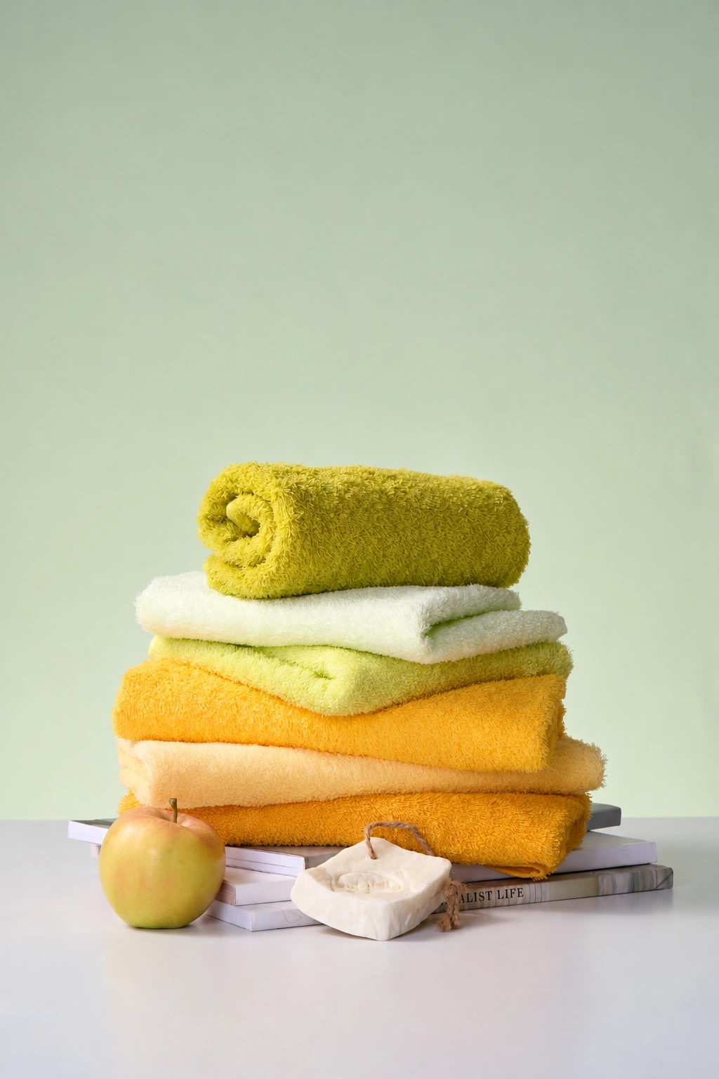 Yellow and cream towels arranged with an apple and soap against a soft green background.