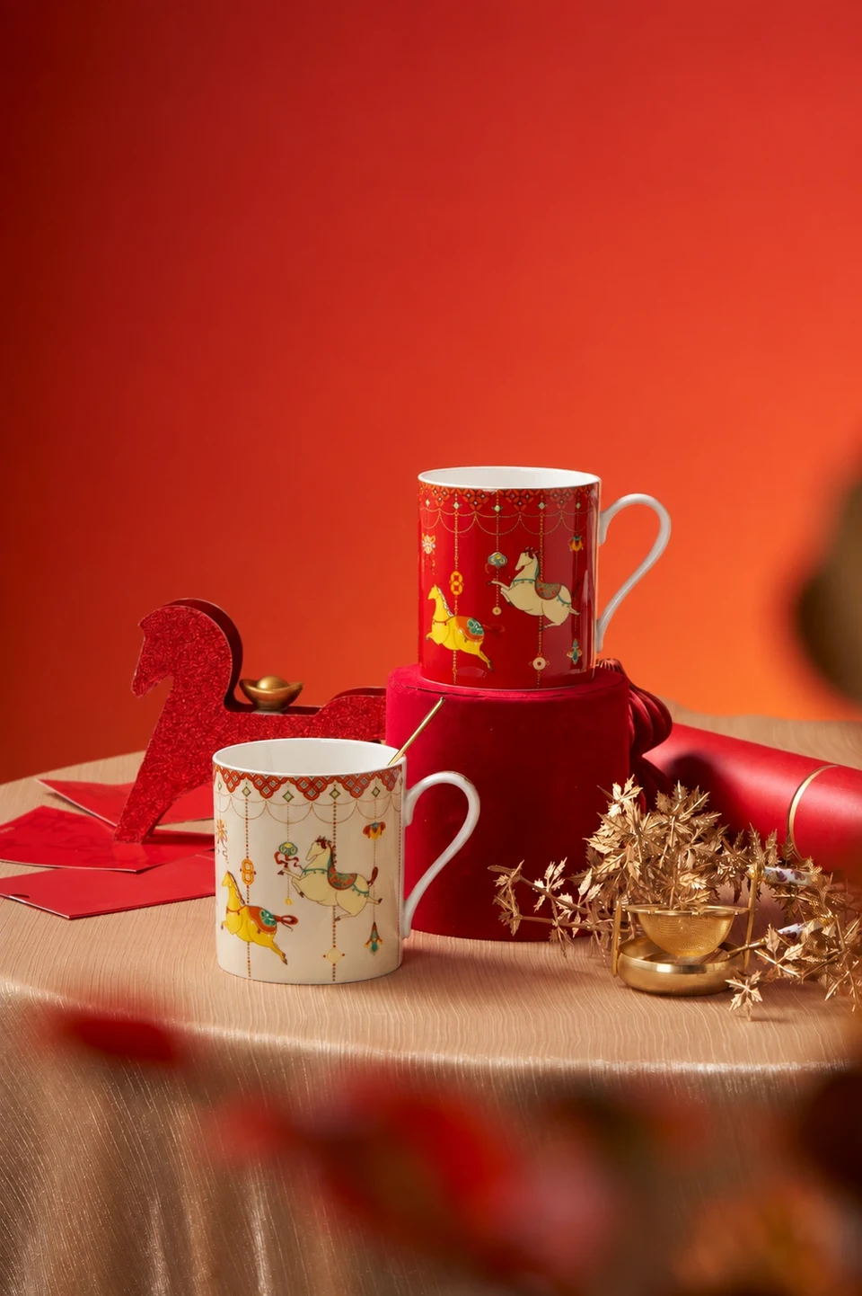 Decorated ceramic mugs styled with red and gold festive props.