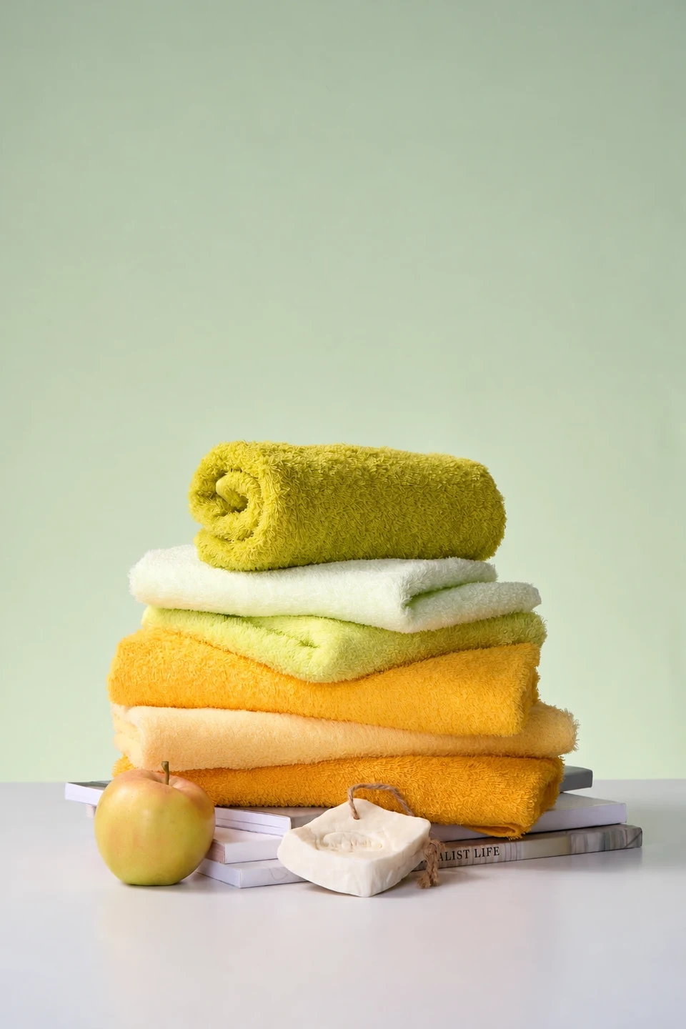 Yellow and cream towels arranged with an apple and soap against a soft green background.
