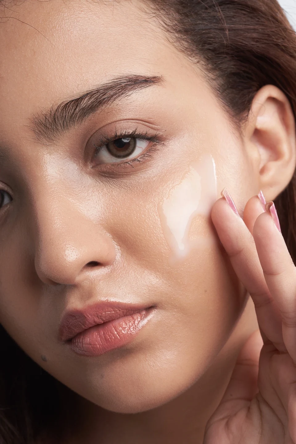 A close-up beauty portrait showing skincare cream applied to the cheek.