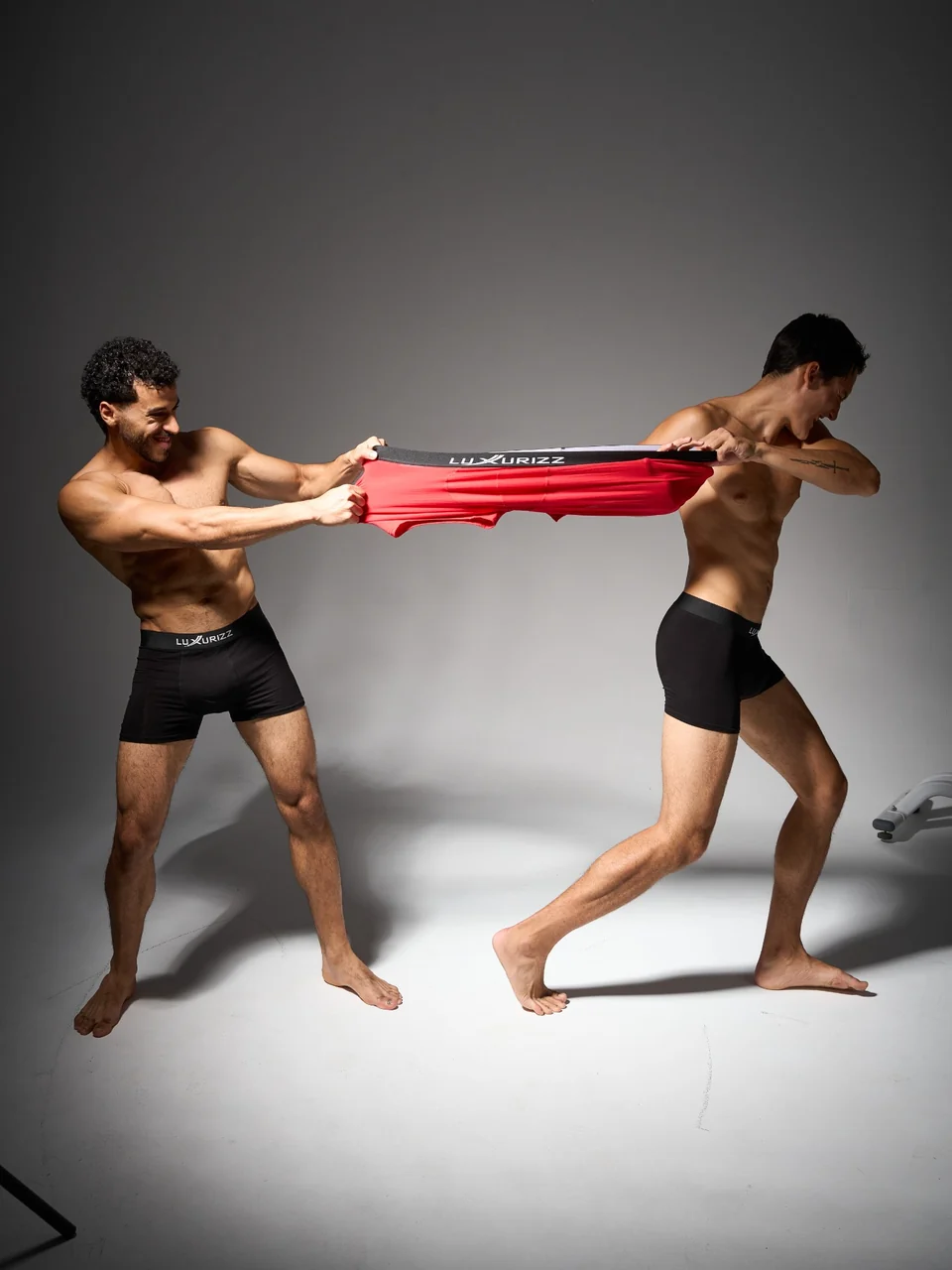 Two models demonstrate the stretch of red Luxurizz underwear in a studio fashion shoot.