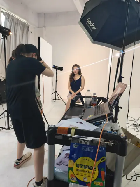 A photographer and softbox positioned around a model for a studio shoot.